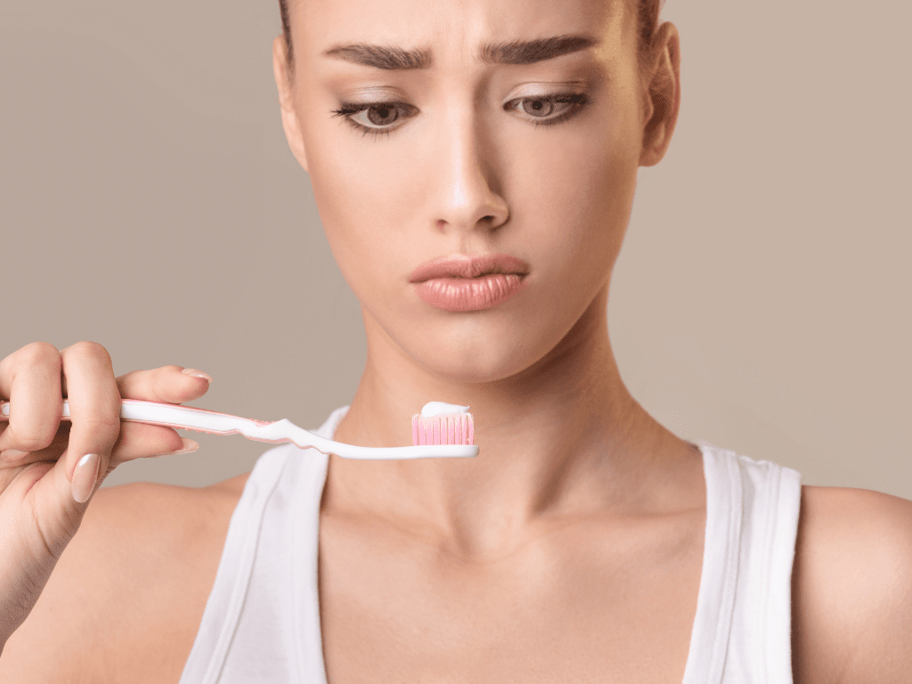 femeie care se uita la o periuta de dinti cu pasta de dinti aplicata
