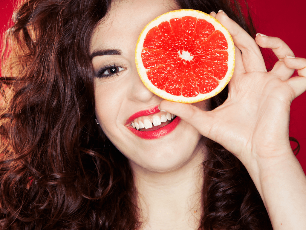 femeie cu strungareata care zambeste si isi acopera unul dintre ori cu o felie de grepfruit
