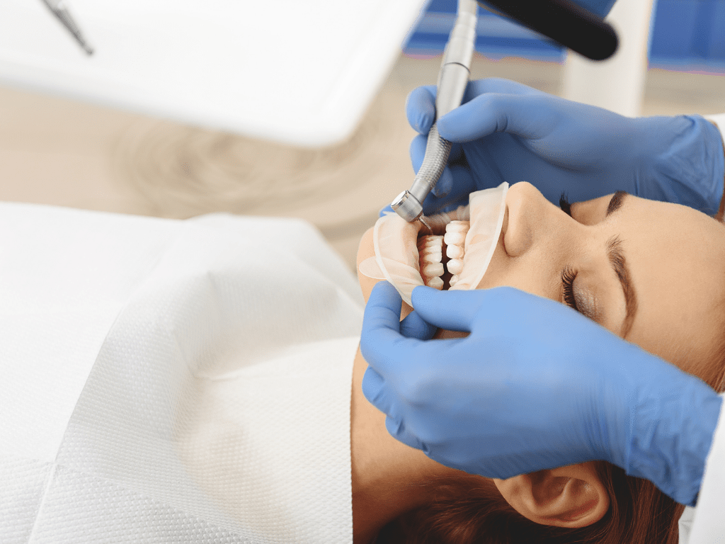 femeie cu gura deschisa caruia medicul stomatolog ii aplica un tratament